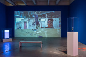 It’s in the Game. 2017. 16:32. 1-channel video (loop, color, sound) with 2 monitors in vitrines on pedestals, Rosco Chroma Key blue paint, orange extension cords. Image courtesy the artist and Bridget Donahue Gallery. © the artist. Photo Credit: Constance Mensh.
